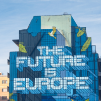 Eine Hochhauswand vor blauem Himmel, die ein Graffiti des Schriftzugs "The Future ist Europe" in blauen Farbtönen trägt