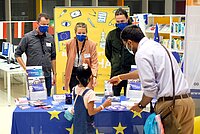 Info-Stand mit Europa-Flaggen und jungen Menschen. Die Menschen tragen Mundschutz (Corona)